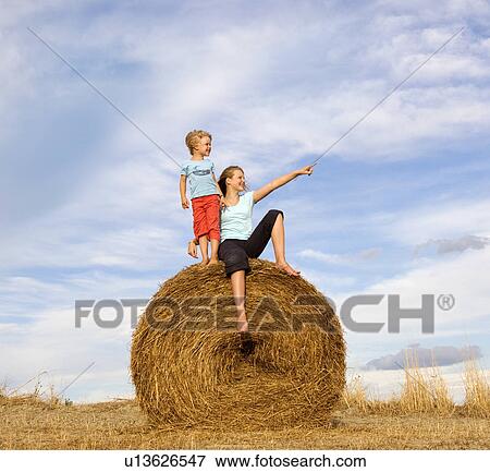 Stock Photo - girl and boy standing on hay bale. Fotosearch