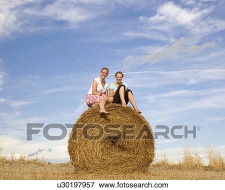 Stock Photo - girl and woman sitting on hay bale. Fotosearch