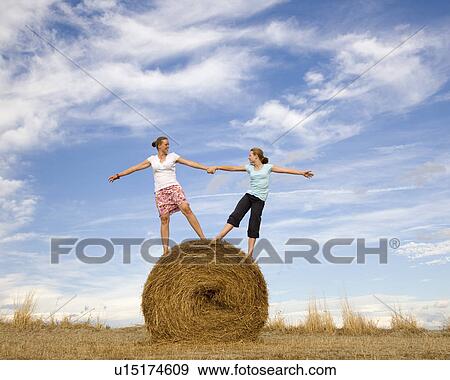 Stock Photo - girl and woman standing on hay bale. Fotosearch