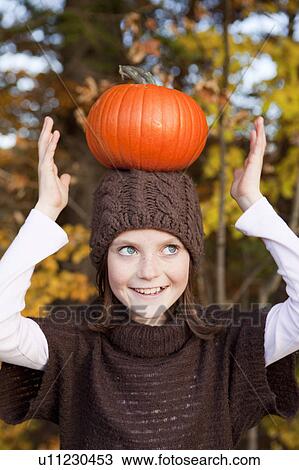 Stock Image - Girl balancing a pumpkin on her head. Fotosearch