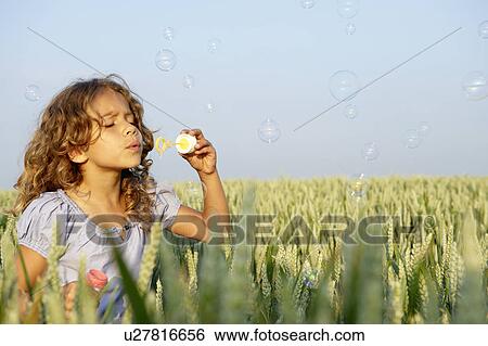 Stock Photograph - Girl blowing bubbles in a wheat field. Fotosearch