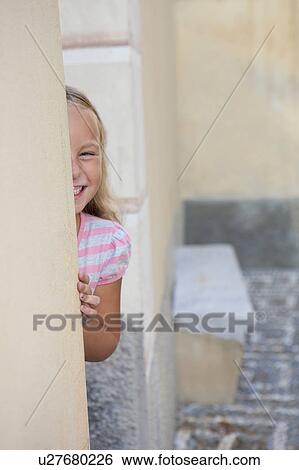 Stock Photograph - girl hiding behind wall, laughing. Fotosearch