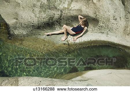 Stock Photo - Girl lying on rock next to stream. Fotosearch