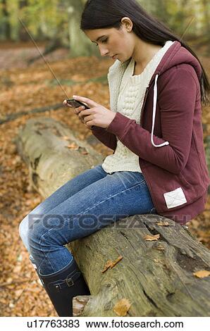 Stock Image - girl on phone on log. Fotosearch