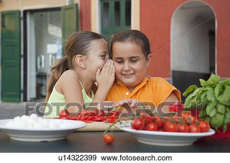Stock Photo - girls whispering whilst preparing food. Fotosearch