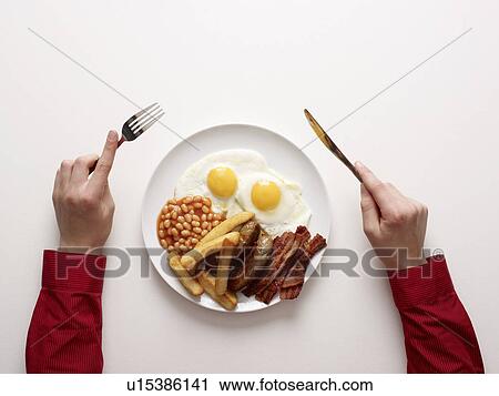 Stock Image - hands next to a fried breakfast. Fotosearch