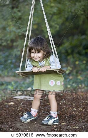 Stock Photograph - Little girl playing on wood swing. Fotosearch