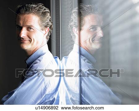 Stock Image - Man against window, smiling. Fotosearch