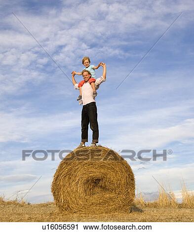Stock Image - man and boy standing on hay bale. Fotosearch
