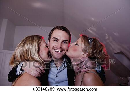 Stock Photo - man being kissed by two women. Fotosearch