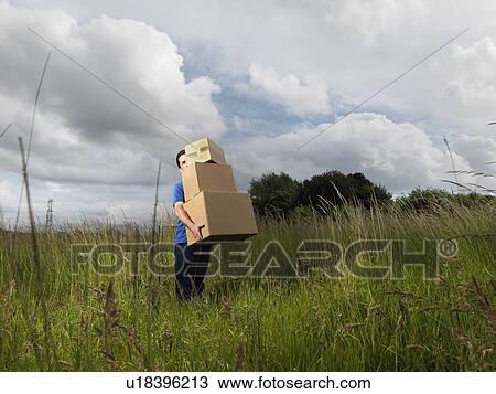 Stock Image - man carrying boxes through field. Fotosearch