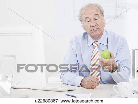 Man looking doubtfully at an apple View Large Photo Image Stock Photo - Man looking doubtfully at an apple. Fotosearch
