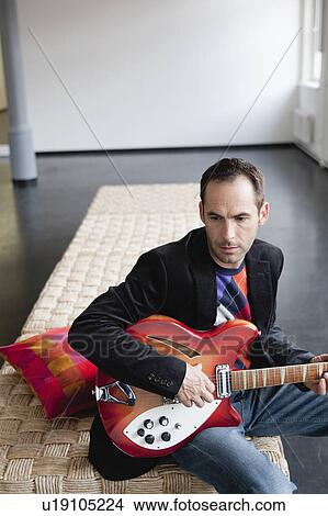 Picture - man playing guitar on bed. Fotosearch