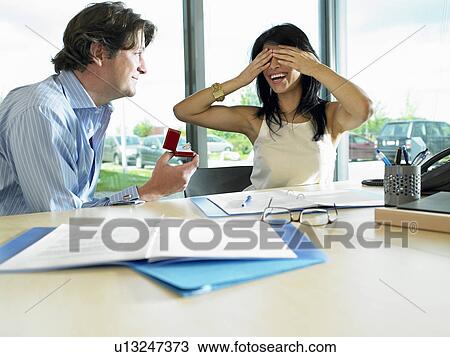 Stock Image - Man proposing to woman, at work. Fotosearch