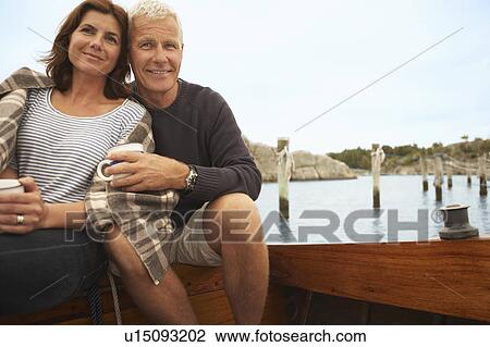 Stock Image - Middle aged couple cuddling on old boat. Fotosearch