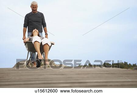 Stock Image - Middle aged woman pushed in wheel barrow. Fotosearch