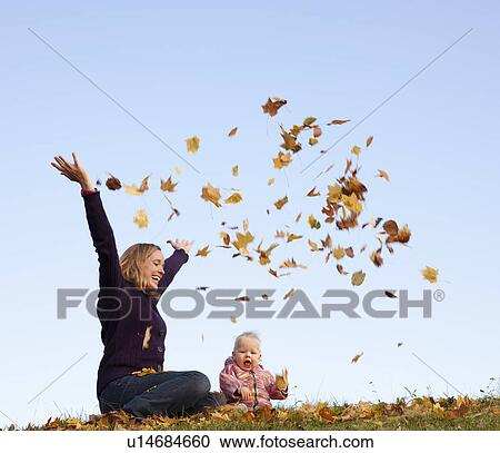 Stock Image - mother and baby throwing autumn leaves. Fotosearch