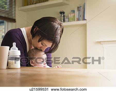 Stock Image - Mother kissing her baby in the kitchen. Fotosearch