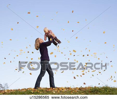 Stock Photography - mother lifting baby in flying leaves. Fotosearch