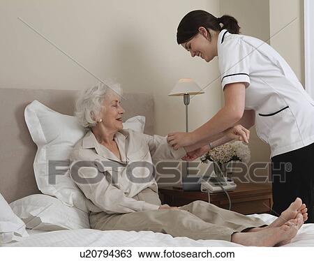 Stock Image - Nurse rolling up elderly woman's sleeve. Fotosearch