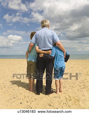 Stock Image - Senior man and 2 boys looking out to sea. Fotosearch
