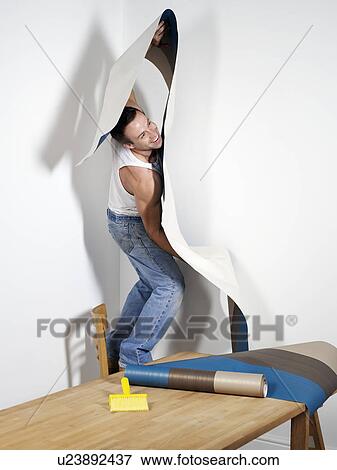 Stock Photo - Smiling man struggling with wallpaper. Fotosearch