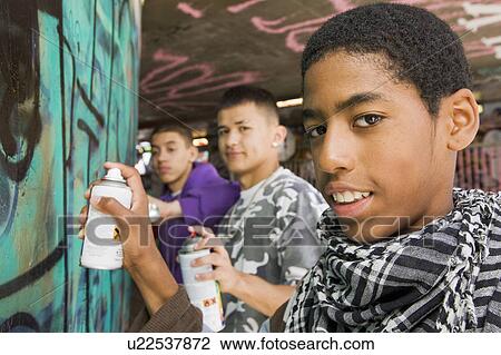 Stock Image - Teenage gang doing graffiti on a wall. Fotosearch