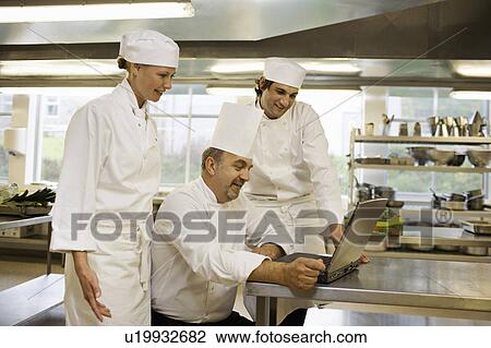 Stock Image - Three chefs looking at a laptop. Fotosearch