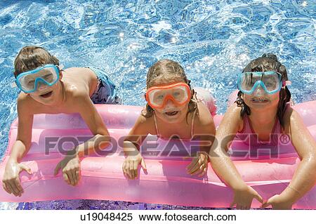 Stock Photography - Three kids on a inflatable in a pool. Fotosearch