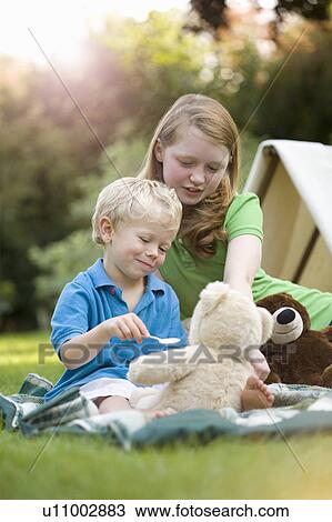 Stock Image - Two children feeding a toy bear. Fotosearch