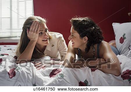 Stock Image - two women laying on bed talking. Fotosearch