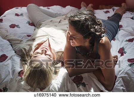 Stock Image - two women laying on bed talking. Fotosearch