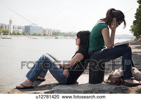 Two women sitting by river View Large Photo Image Stock Image - Two women sitting by river. Fotosearch