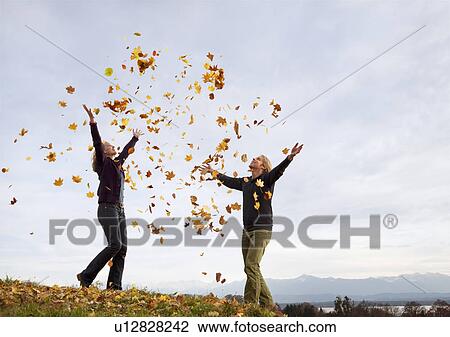 Stock Image - woman and man throwing autumn leaves. Fotosearch