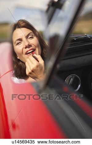 Stock Photography - Woman applying lipstick in cars mirror. Fotosearch