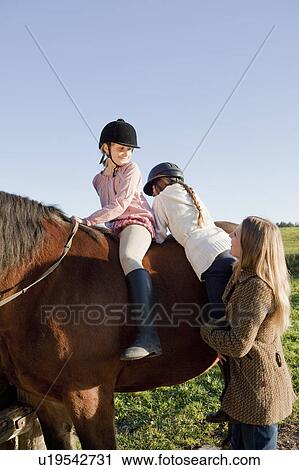 Woman helping girls on horseback View Large Photo Image Stock Image - Woman helping girls on horseback. Fotosearch