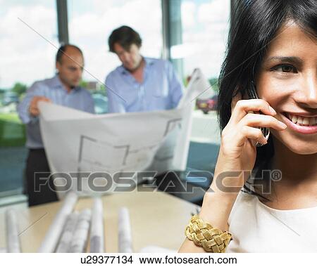 Picture - Woman on the phone, men with blue prints. Fotosearch