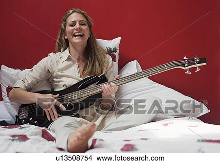 Picture - woman playing guitar on bed. Fotosearch