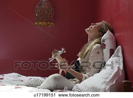 Stock Image - woman playing guitar on bed. Fotosearch
