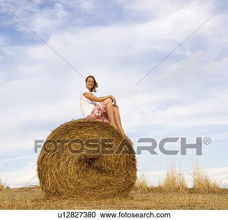 Stock Image - woman sitting on hay bale. Fotosearch