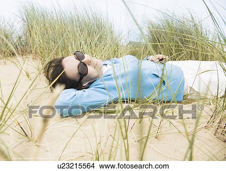 Picture - Woman with sunglasses lying in dunes. Fotosearch