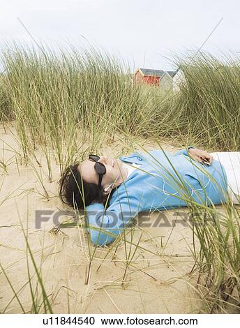 Stock Image - Woman with sunglasses lying in dunes. Fotosearch