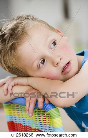 Stock Photograph - young boy resting head on back of chair. Fotosearch