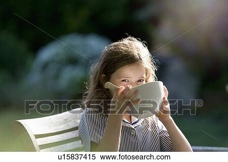 Stock Photography - Young girl drinking from bowl in garden. Fotosearch