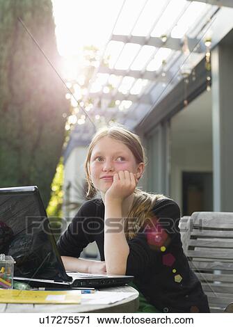 Stock Image - Young girl thinking at laptop in garden. Fotosearch