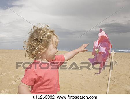 Stock Image - Young girl with windmill on beach. Fotosearch