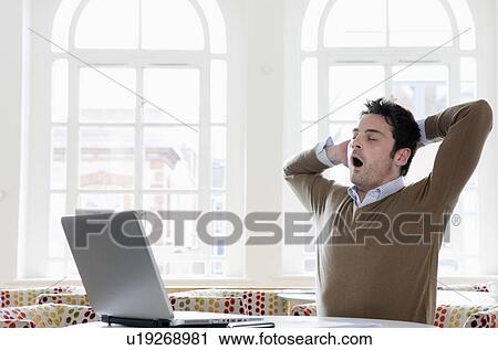 Young man yawning at office View Large Photo Image Stock Image - Young man yawning at office. Fotosearch