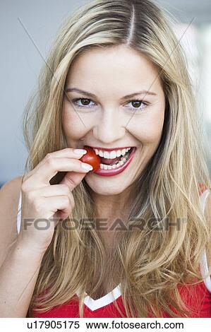 Stock Photography - Young woman nibbling on tomato. Fotosearch