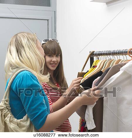 Stock Photo - 2 young women standing at clothes rail. Fotosearch