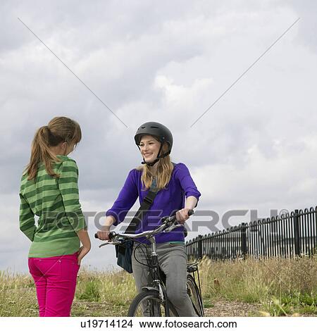 Picture - 2 young women with bicycle chatting. Fotosearch
